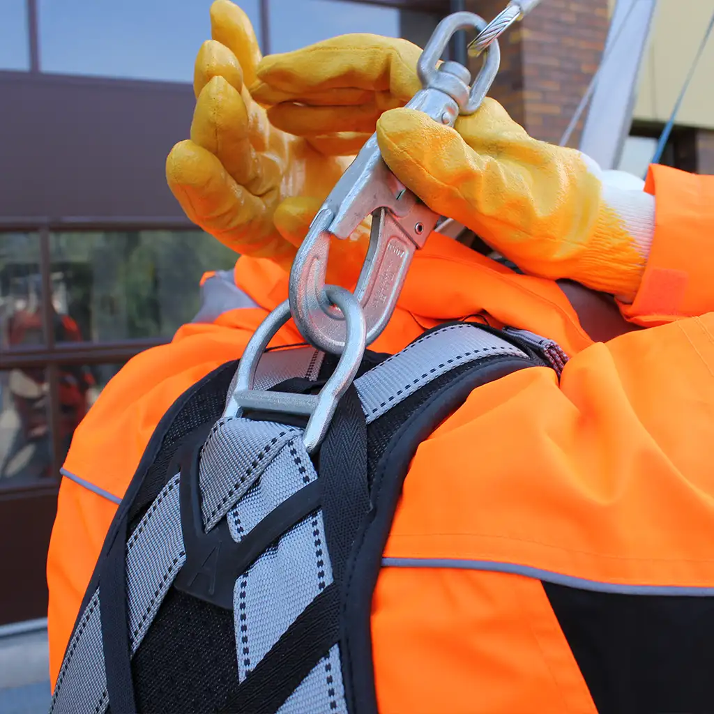 Ein Arbeiter in Schutzkleidung befestigt einen Absturzhaken am Rücken.